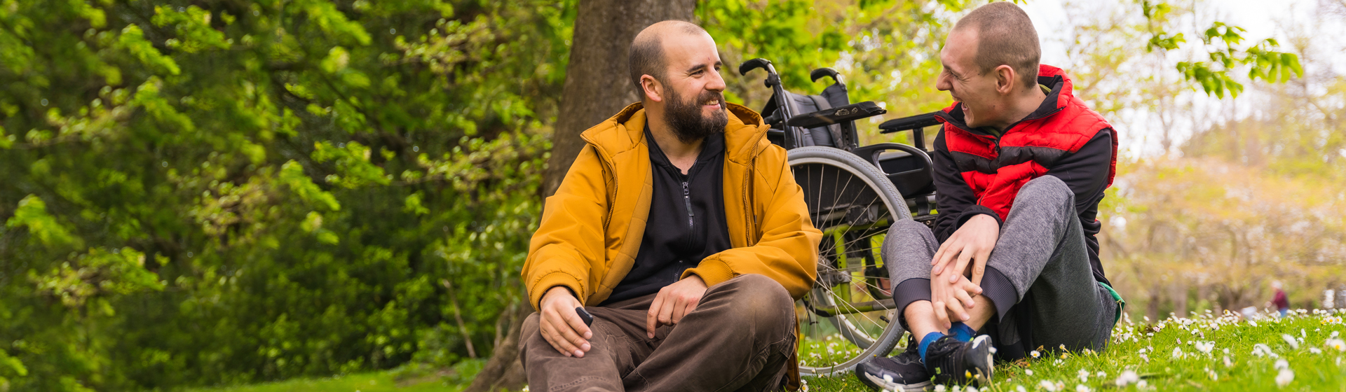 Two men smiling outside next to a wheelchair